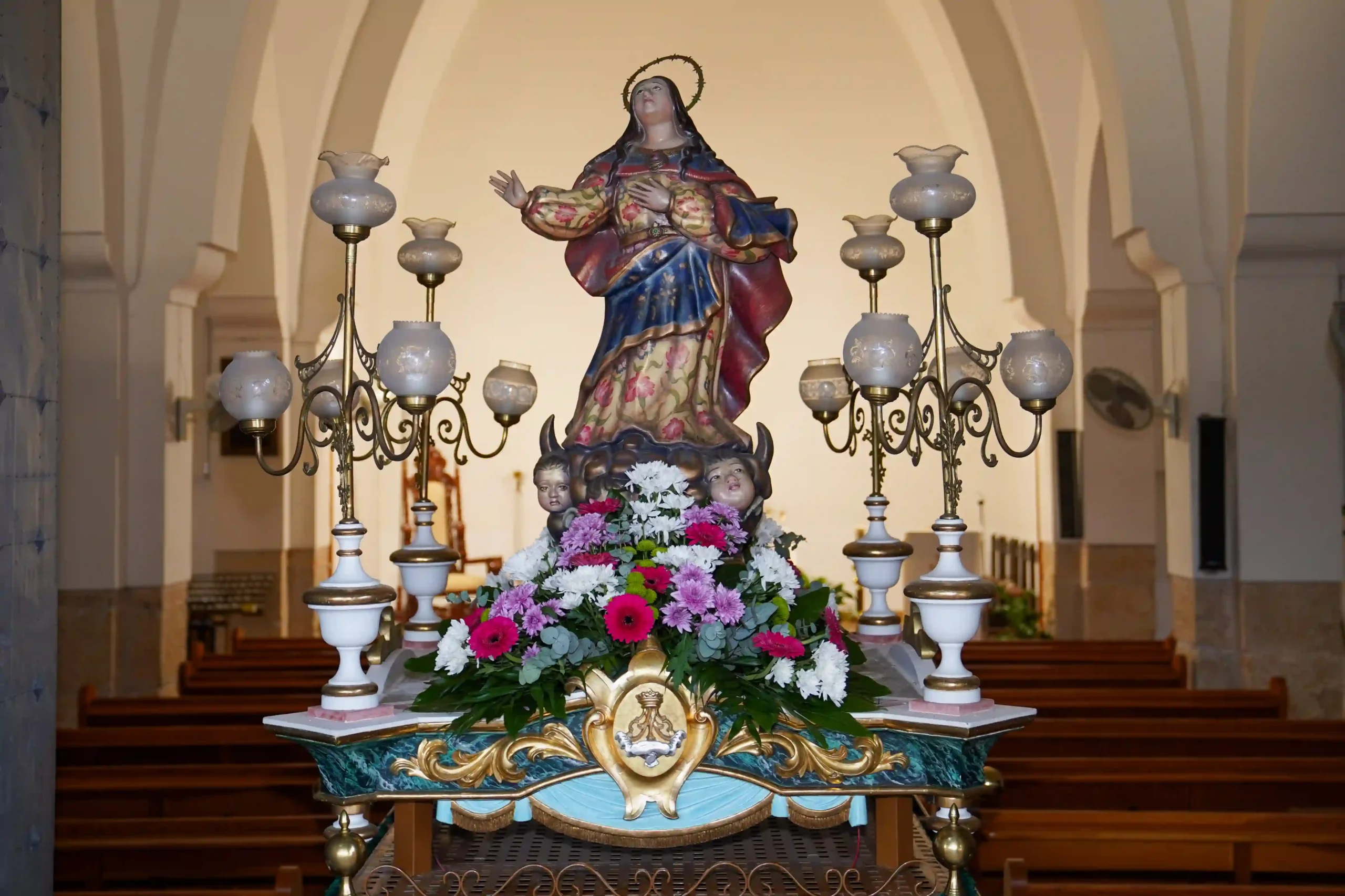 Imagen de la Mare de Déu del Mondúver vestida con manto bordado sobre altar decorado con flores y candelabros en el interior de la iglesia de Marxuquera durante la Romería 2025