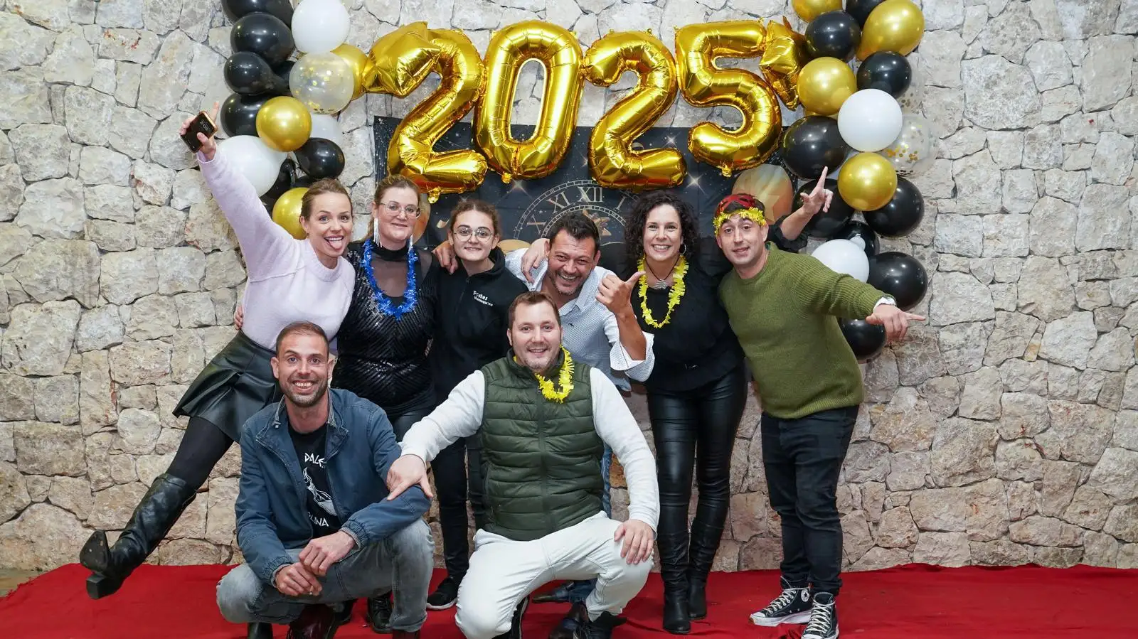 Miembros de la comisión de Festes de Marxuquera posando alegres bajo el cartel de 2025 durante la fiesta de Fin de Año