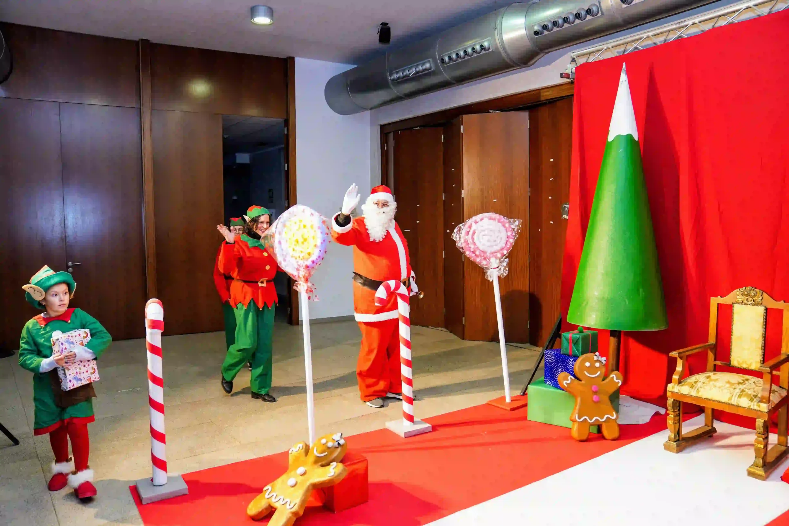 Papá Noel y los elfos saludando al público al llegar al escenario del Centro Social decorado con bastones de caramelo