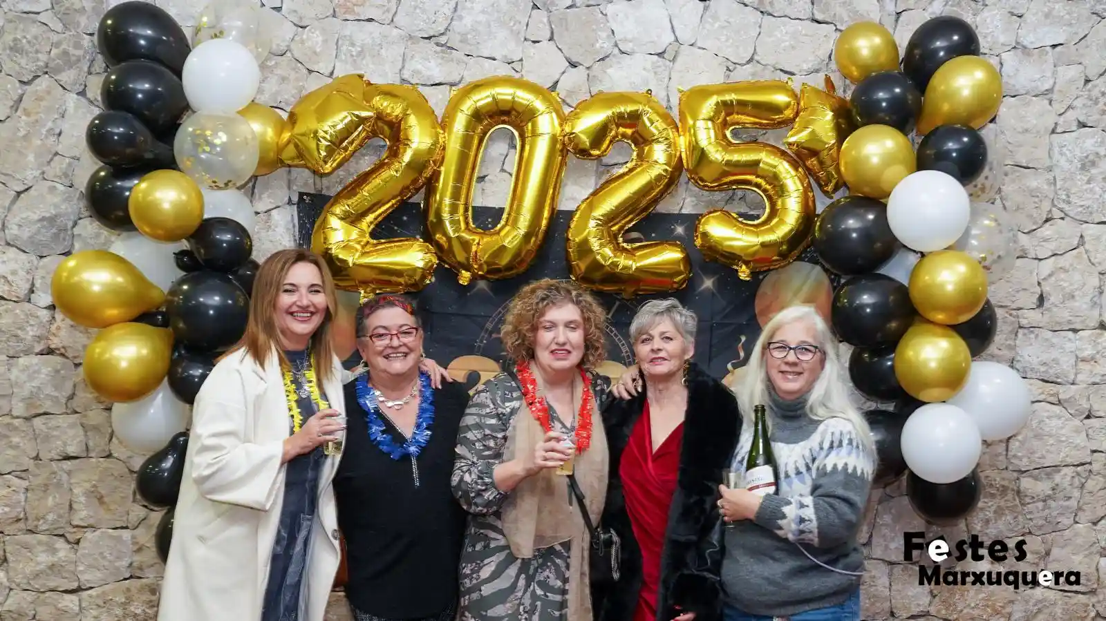 Cinco mujeres celebran el año nuevo en Marxuquera con copas, gorros y serpentinas junto al photocall decorado con globos dorados