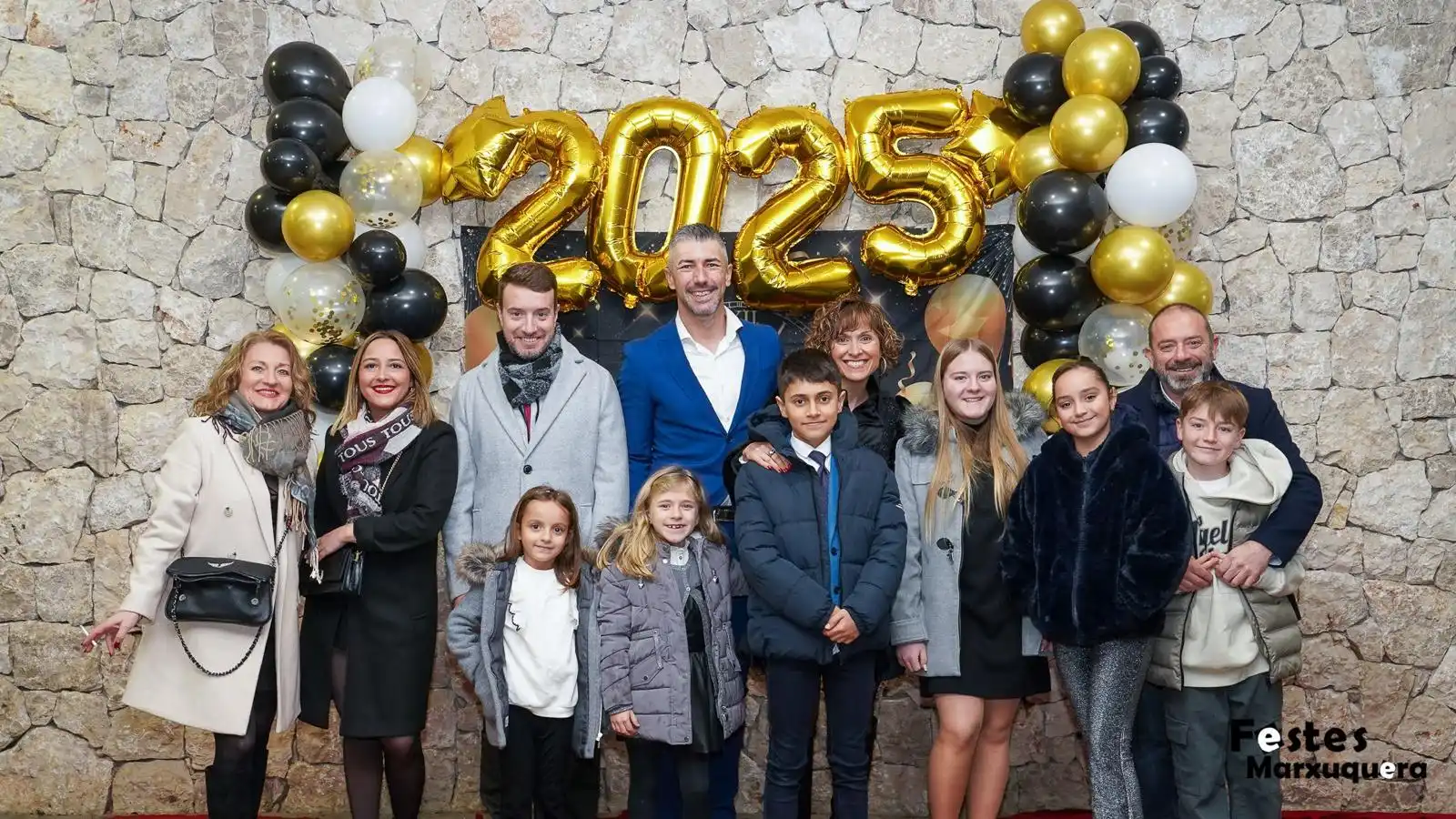 Familia numerosa posando frente al photocall 2025 decorado con globos negros, blancos y dorados en Nochevieja