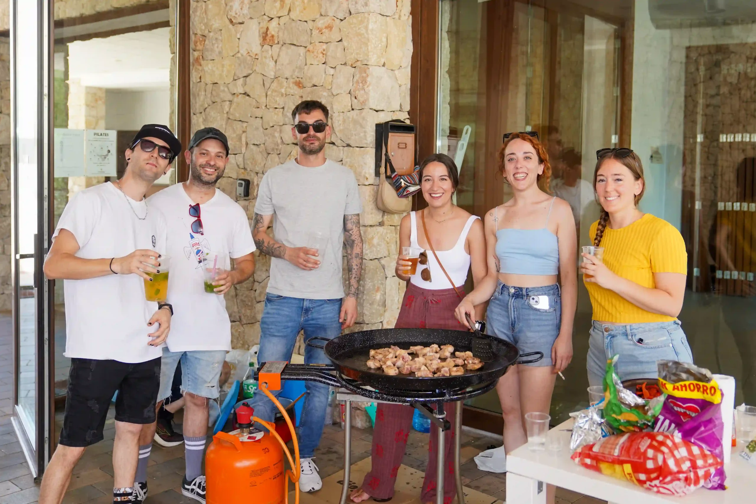 Grupo de seis personas cocinando paella y compartiendo bebidas y snacks durante la Romería a la Mare de Déu del Mondúver 2025 en Marxuquera