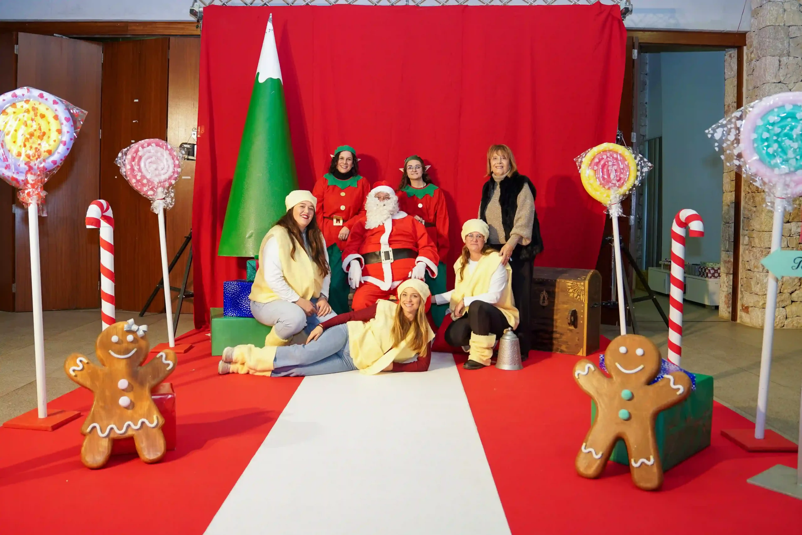 Mujeres disfrazadas de pastoretes posan con Papá Noel en el escenario decorado del evento navideño