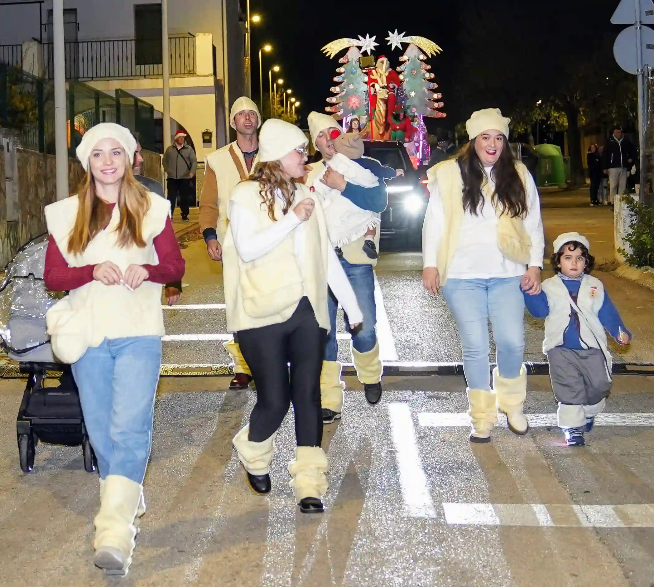 Pastoretes y niños caminando delante de la carroza iluminada de Papá Noel durante el desfile navideño