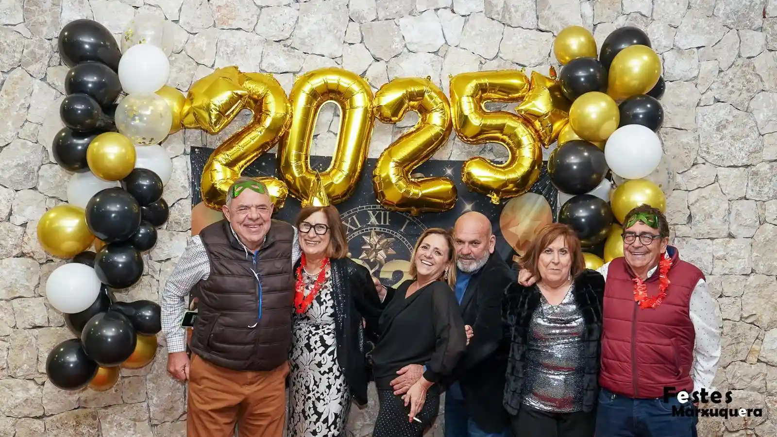 Hombres y mujeres posan juntos bajo los globos dorados y decoración festiva de la Nochevieja 2024 en Marxuquera