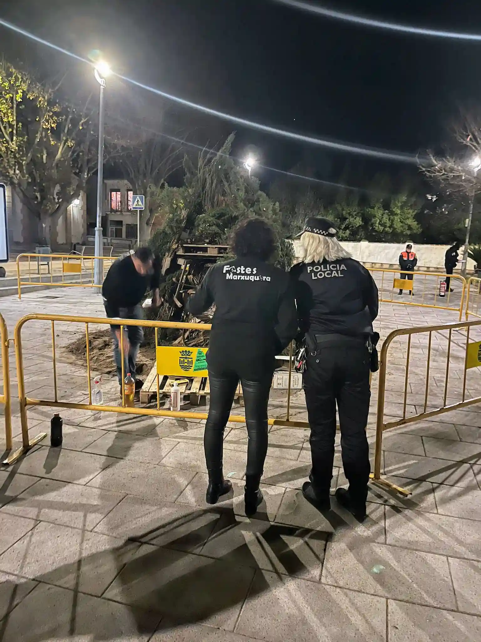 Policía local junto a una miembro de la comisión revisando la hoguera antes de encenderla en Sant Antoni 2025.